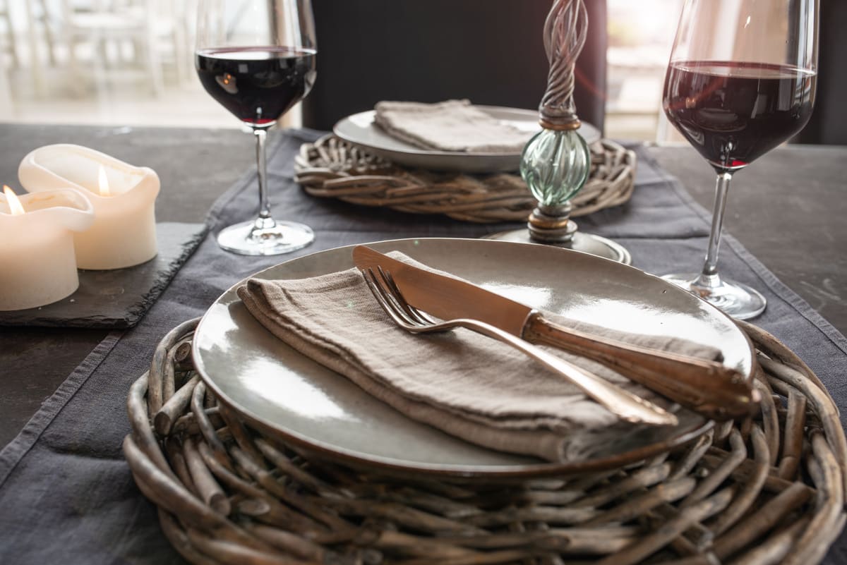 Festlich rustikaler Tisch mit Stoffserviette, Wein und Platzteller aus Korb